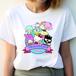 May include: White t-shirt with a colorful graphic of cartoon characters playing sports. The graphic includes the text "Friendship Team".