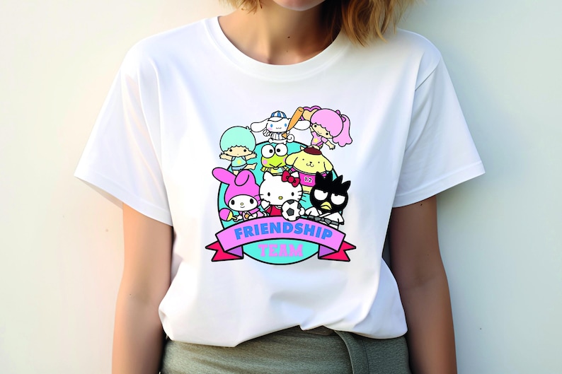May include: White t-shirt with a colorful graphic of cartoon characters playing sports. The graphic includes the text "Friendship Team".