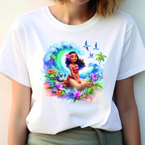 Peut inclure: T-shirt blanc avec un imprim&eacute; graphique color&eacute; de Moana du film Disney Moana. Le graphique repr&eacute;sente Moana assise sur un rocher avec une vague derri&egrave;re elle, entour&eacute;e de fleurs tropicales et d'oiseaux.