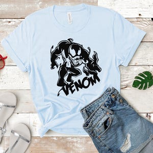 May include: A light blue t-shirt with a black graphic of Venom, a Marvel Comics character, with the word "VENOM" printed below the graphic.
