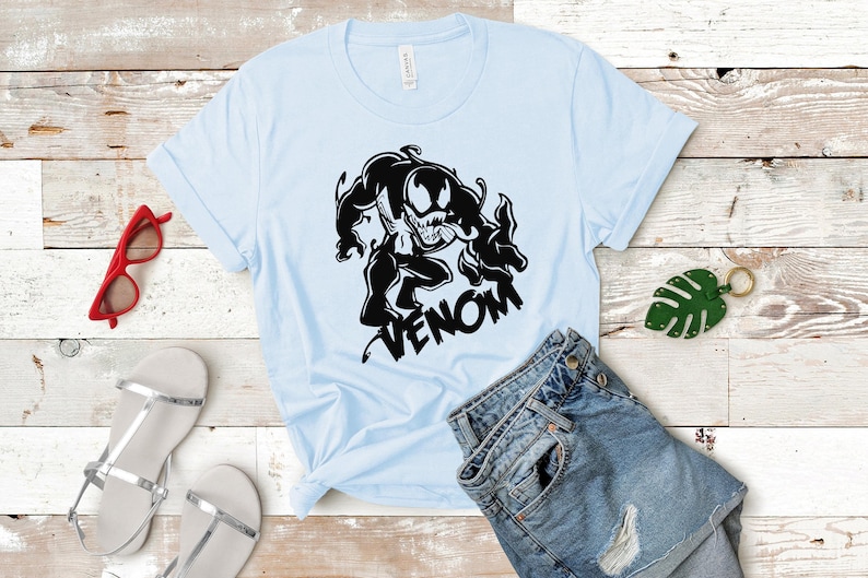 May include: A light blue t-shirt with a black graphic of Venom, a Marvel Comics character, with the word "VENOM" printed below the graphic.