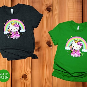 May include: Two short-sleeved t-shirts, one heather dark grey and one kelly green. Each shirt features a cartoon image of a princess cat with a rainbow, crown, and wand. The cat is wearing a pink dress.