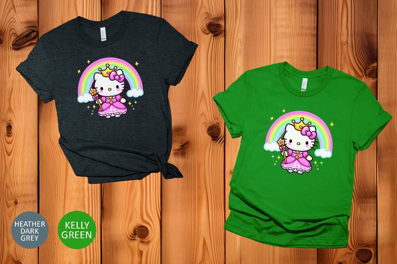 May include: Two short-sleeved t-shirts, one heather dark grey and one kelly green. Each shirt features a cartoon image of a princess cat with a rainbow, crown, and wand. The cat is wearing a pink dress.