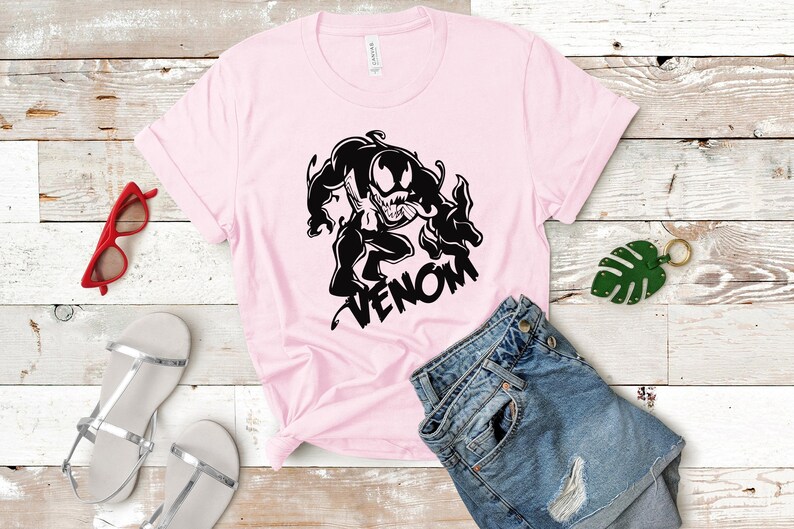 May include: A pink t-shirt with a black graphic of Venom, a fictional superhero, with the word "VENOM" printed below the graphic.