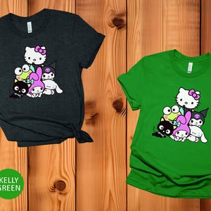 K&ouml;nnte beinhalten: Zwei T-Shirts mit einem Grafikdruck von Hello Kitty und ihren Freunden. Das linke Shirt ist dunkelgrau meliert und das rechte Shirt ist kellygr&uuml;n.