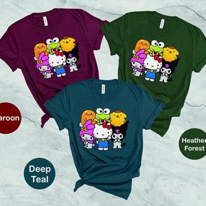 May include: Three t-shirts featuring a group of cartoon characters including Hello Kitty and a frog. The t-shirts are in maroon, deep teal and heather forest.