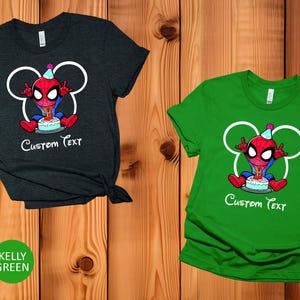May include: Two t-shirts, one heather dark grey and one kelly green, with a cartoon Spider-Man design and a birthday cake. The design includes white Mickey Mouse ears and the words "Custom Text".