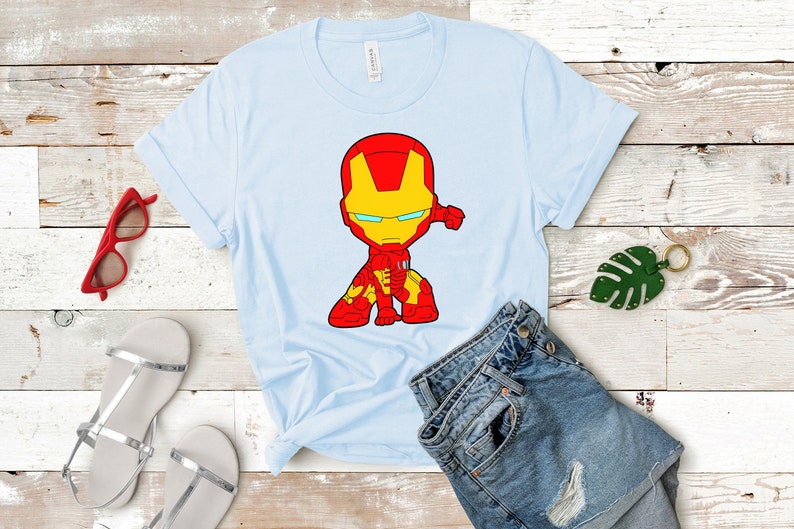 Puede incluir: Una camiseta azul claro con una imagen de dibujos animados de Iron Man con un traje rojo y amarillo. La imagen est&aacute; centrada en la camiseta.