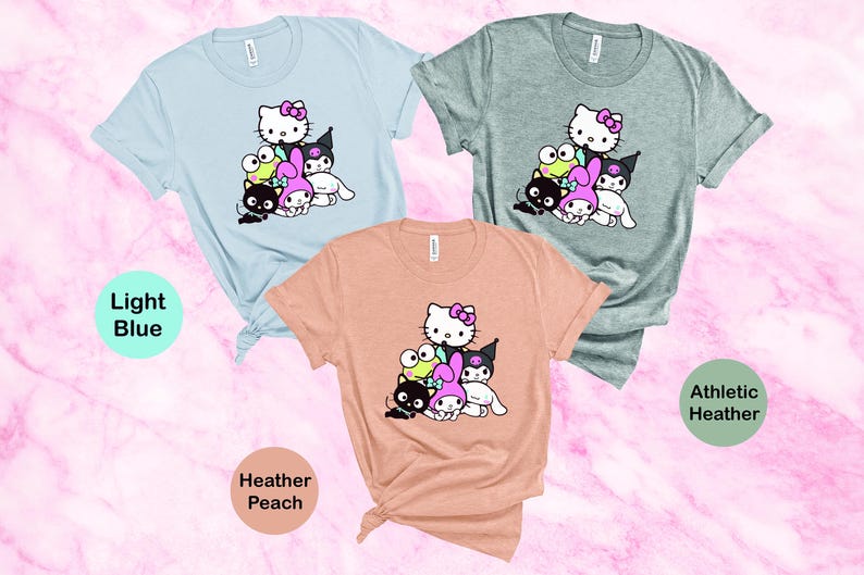K&ouml;nnte beinhalten: Drei T-Shirts mit einem Grafikdruck von Hello Kitty und ihren Freunden. Die T-Shirts sind in hellblau, heidefarbenem Pfirsich und sportlichem Grau.