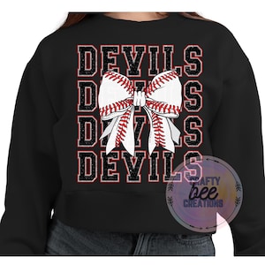 May include: Black cropped sweatshirt with the word "DEVILS" repeated four times in a glittery font. A white and red baseball-themed bow is centered between the words.