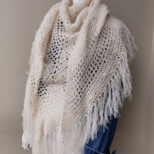 May include: A white crocheted shawl with fringe. The shawl is draped over a mannequin wearing a denim shirt.
