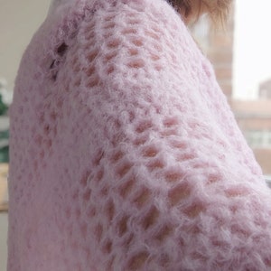 May include: A close-up of a soft, pink, fuzzy sweater with a delicate open-stitch pattern.