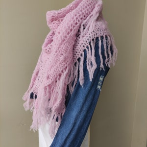 May include: A pink crocheted shawl with fringe. The shawl is draped over a denim jacket.