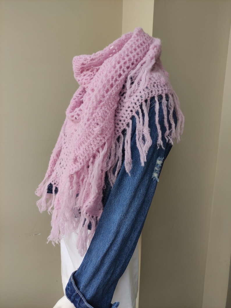 May include: A pink crocheted shawl with fringe. The shawl is draped over a denim jacket.