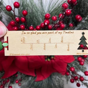 May include: A wooden Christmas ornament with a timeline design. The ornament features the text "I'm so glad you are part of my Timeline" and a small Christmas tree with the text "Merry Christmas".