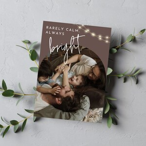 May include: A Christmas card featuring a photograph of a family of four, with the text "Rarely Calm, Always Bright" and fairy lights.