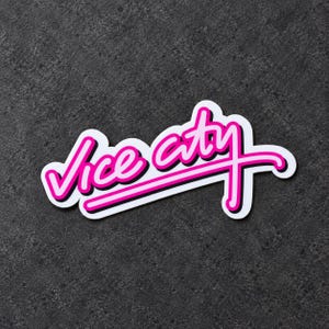 May include: A die-cut sticker featuring the text Vice City in a bright pink script font with a thick black outline and a white border. The lettering has a stylized underline that extends from the letter y across the bottom of the word.
