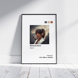 May include: A framed art print with the text "Weisses Herz" and "Ayliva". The artwork features a portrait of a person. The release date "24. März 2022" is displayed. The print is set against a white background.
