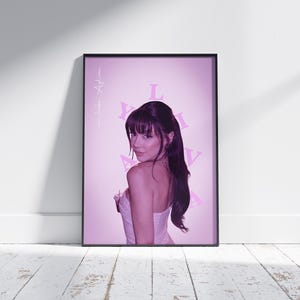May include: A pink and white poster featuring a woman with dark hair and bangs, wearing a white strapless top. The background is a light pink with the word "LIL" in pink letters.