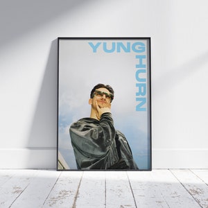 May include: A black framed poster with a photo of a person wearing sunglasses and a dark green jacket. The text "YUNG HURN" is printed in blue on the right side of the poster.