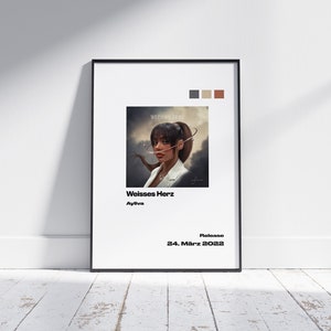 May include: A white poster with black text and a color palette of gray, brown, and beige. The poster features a photo of a woman with a ponytail, wearing a white jacket and looking at the camera. The text on the poster reads "Weisses Herz" and "Ayliva". The release date is "24. März 2022".