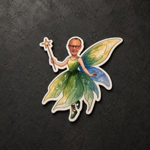May include: A die-cut sticker featuring a watercolor illustration of a fairy with a person's face wearing glasses. The fairy wears a green leaf-patterned dress and matching shoes, holding a gold star-tipped wand with large yellow and blue wings.