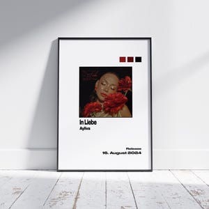 May include: A black and white poster featuring a woman's face in the centre. The woman is surrounded by red flowers. The text "In Liebe" and "Ayliva" is below the image. The text "Release 16. August 2024" is at the bottom of the poster.