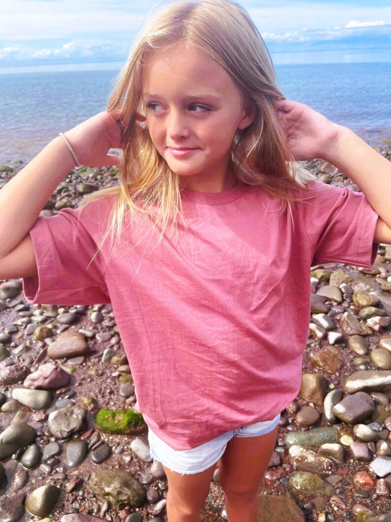Peut inclure: Une jeune personne portant un t-shirt rose et un short en jean debout sur une plage rocheuse.