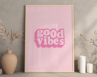 May include: A framed pink art print with the words "good vibes" in a retro font. The artwork is displayed on a shelf with decorative vases, candles, and dried plants. The overall aesthetic is modern and minimalist.