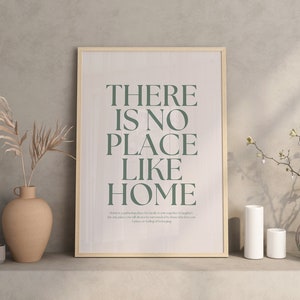 May include: A framed print with the text "There is no place like home" in a green font on a white background. The print is on a shelf with a vase of dried branches, two candles, and a vase of white flowers.