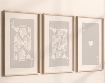 May include: Three framed prints of playing cards, each featuring a different card from the heart suit: the Jack, King, and Ace. The cards are printed in white on a light gray background.