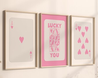 May include: Three framed art prints featuring playing card designs. The prints include an Ace of Hearts, a Queen of Hearts with the text "LUCKY YOU", and an Eight of Hearts. The cards are in pink on a cream background.