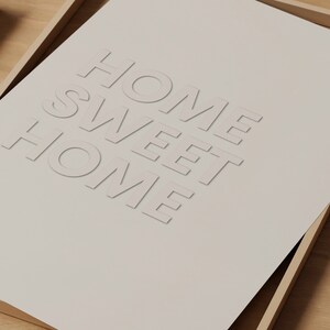 May include: A framed print with the text "Home Sweet Home" in a white, raised font on a beige background.
