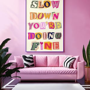 May include: A pink sofa with white and black striped pillows in front of a pink wall with a framed print that reads "Slow Down You're Doing Fine".