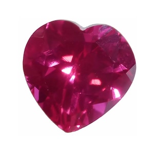 May include: A faceted, heart-shaped gemstone in a vibrant shade of magenta. The gem's surface reflects light, showcasing its multiple facets and creating a sparkling effect. The heart shape is clearly defined, with a smooth, rounded top and pointed base.