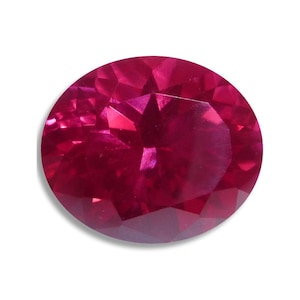 May include: A faceted, oval-shaped ruby gemstone. The gem is a deep, saturated red color with multiple facets that reflect light. The ruby is set against a white background, highlighting its color and brilliance.