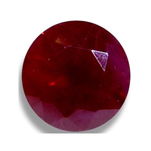 May include: A faceted, round ruby gemstone. The gem is a deep, rich red color with a polished surface. The facets create a play of light and shadow, enhancing the stone's brilliance. The ruby is set against a white background.