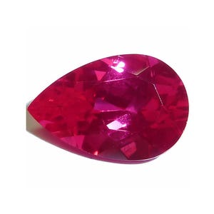 May include: A faceted, pear-shaped ruby gemstone. The gem is a deep, vibrant red color with multiple facets that reflect light. The gemstone is set against a white background.