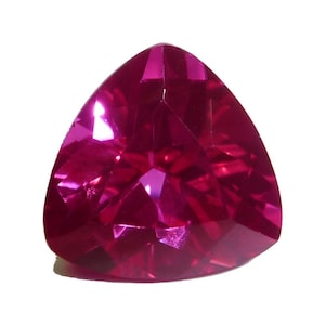 May include: A faceted, triangular-shaped gemstone with a deep magenta hue. The gem's surface reflects light, showcasing its multiple facets and internal structure. The stone is set against a white background, highlighting its color and shape.