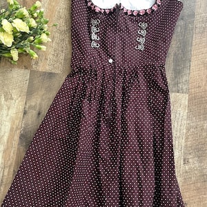 Könnte beinhalten: Ein dunkelbraunes Dirndlkleid mit weißen Punkten. Das Kleid hat ein weißes Oberteil mit rosa Besatz und silberfarbenen Verzierungen. Es hat einen Reißverschluss und einen ausgestellten Rock. Der Text "ORIGINAL STENGL" ist sichtbar.
