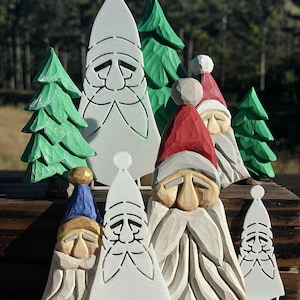 May include: A collection of carved wooden Christmas decorations, including Santa Claus figures and green Christmas trees. The Santa figures have white beards and red or blue hats. The trees are painted green.
