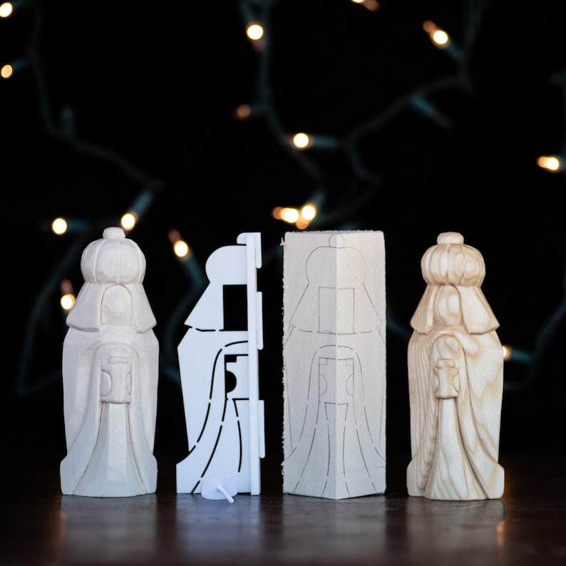 May include: Three wooden figurines of the three wise men, each with a crown and a robe. The figurines are standing on a wooden surface. The figurines are white and have a light wood finish. The figurines are part of a nativity scene.