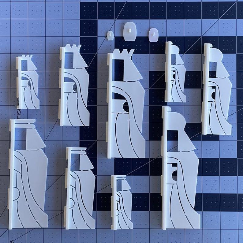 May include: A set of nine white plastic cookie cutters shaped like castles with different designs. The cutters are arranged on a gray grid background.