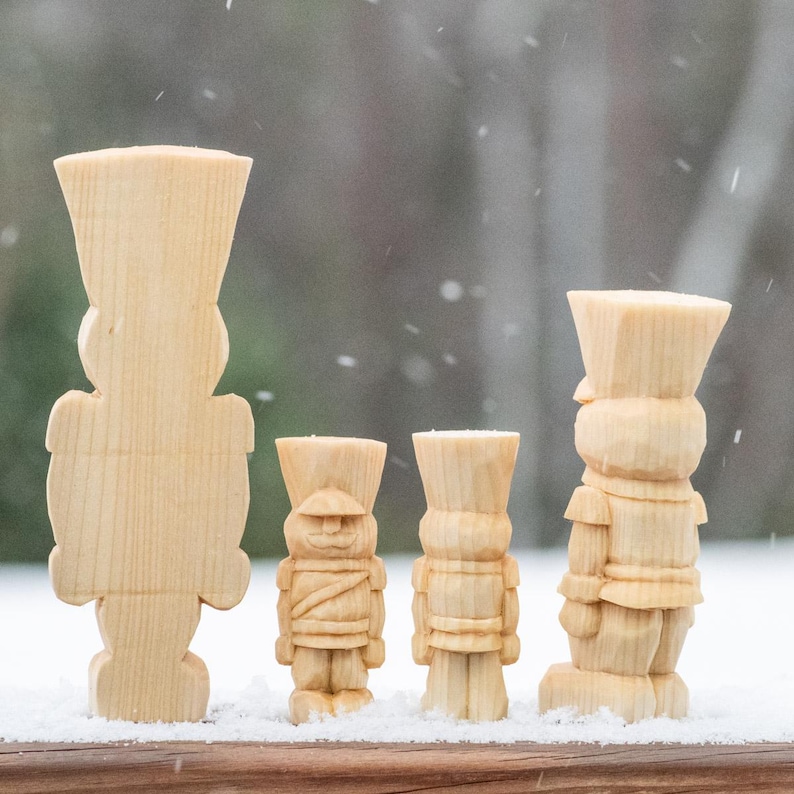 May include: Four wooden nutcracker figurines of varying sizes, standing in a row on a snowy surface. The nutcrackers are all made of unfinished wood and have a simple, traditional design.