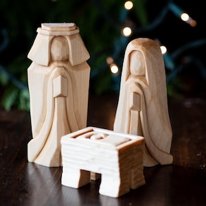 K&ouml;nnte beinhalten: Eine Weihnachtskrippe aus Holz mit drei Figuren: ein K&ouml;nig, eine K&ouml;nigin und eine Krippe. Die Figuren sind aus hellem Holz geschnitzt und haben einfache, stilisierte Z&uuml;ge.