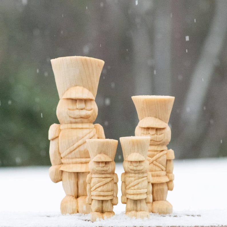 May include: Three wooden toy nutcracker figurines, each with a different size. The largest nutcracker is standing in the center, with a smaller nutcracker on each side. All three nutcrackers are painted in a natural wood color.