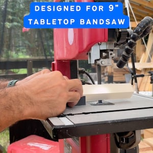 Pode incluir: Uma serra de fita de mesa vermelha e preta com capacidade para lâminas de 22,86 cm. A máquina foi projetada para trabalhar madeira e possui uma mesa de metal e um tubo preto flexível. O texto "DESIGNED FOR 9" TABLETOP BANDSAW" é exibido em um retângulo azul.