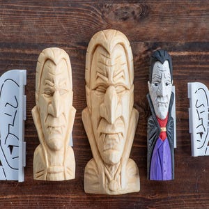 May include: Two unpainted light-colored wooden carvings of vampire busts with pointed ears and high collars, alongside one painted vampire figure with black hair, a white face, a red shirt, and a purple vest, plus two white plastic stencils of the design.
