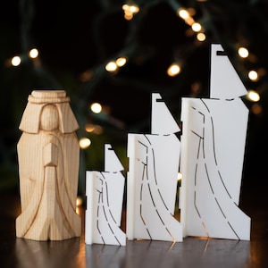 K&ouml;nnte beinhalten: Ein Set aus vier wei&szlig;en Weihnachtsornamenten aus Holz, jedes mit einem einzigartigen Design eines stilisierten Weihnachtsbaums. Die Ornamente sind nach Gr&ouml;&szlig;e geordnet, das gr&ouml;&szlig;te Ornament rechts und das kleinste links. Eine Holzfigur einer Person in einer Robe ist ebenfalls im Bild enthalten.