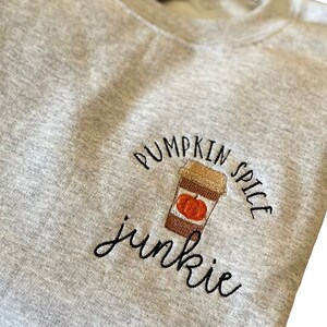 May include: Gray sweatshirt with embroidered text "Pumpkin Spice Junkie" and a stylized image of a coffee cup with a pumpkin inside.